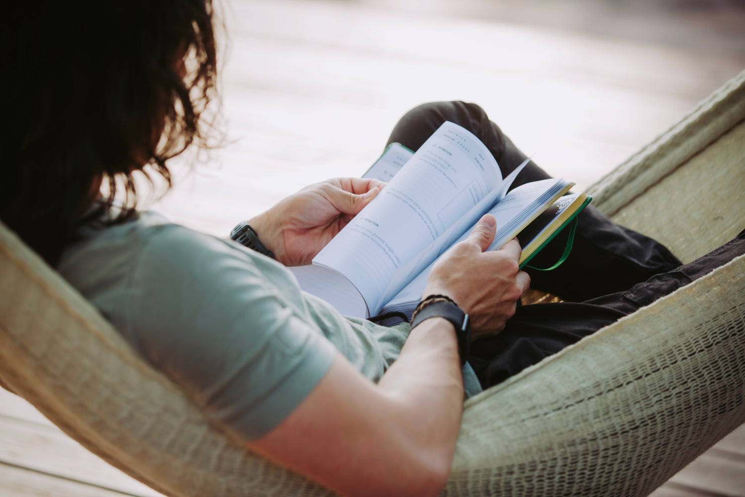 Close-up of a person reading the daily prompts in the Microdose Journal while relaxing in a hammock, emphasizing mindfulness and self-reflection.