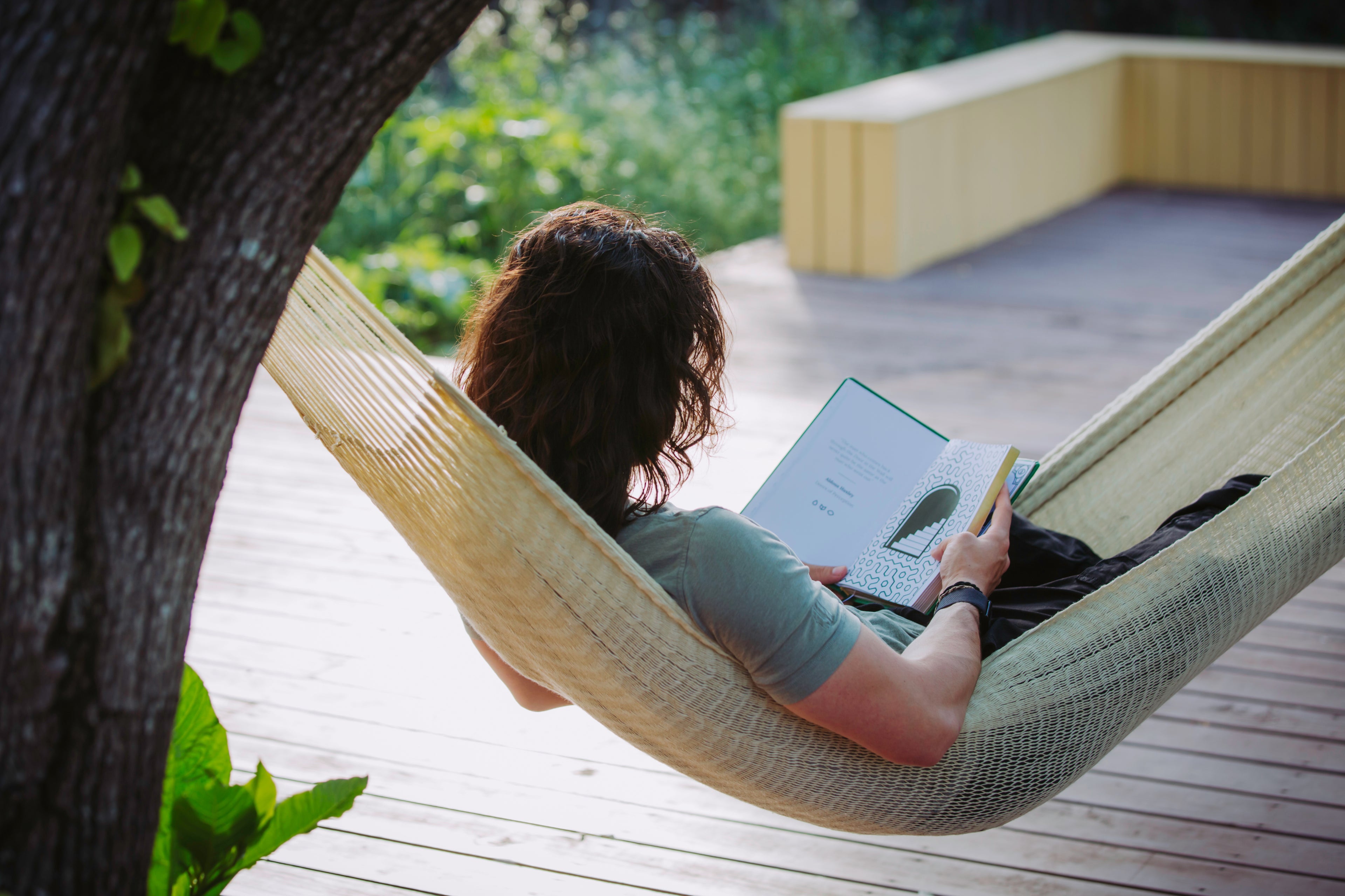 Person relaxing in a hammock outdoors while holding the Microdose Journal open to the decorative endpaper, surrounded by natural light and greenery, embodying mindfulness and creativity.