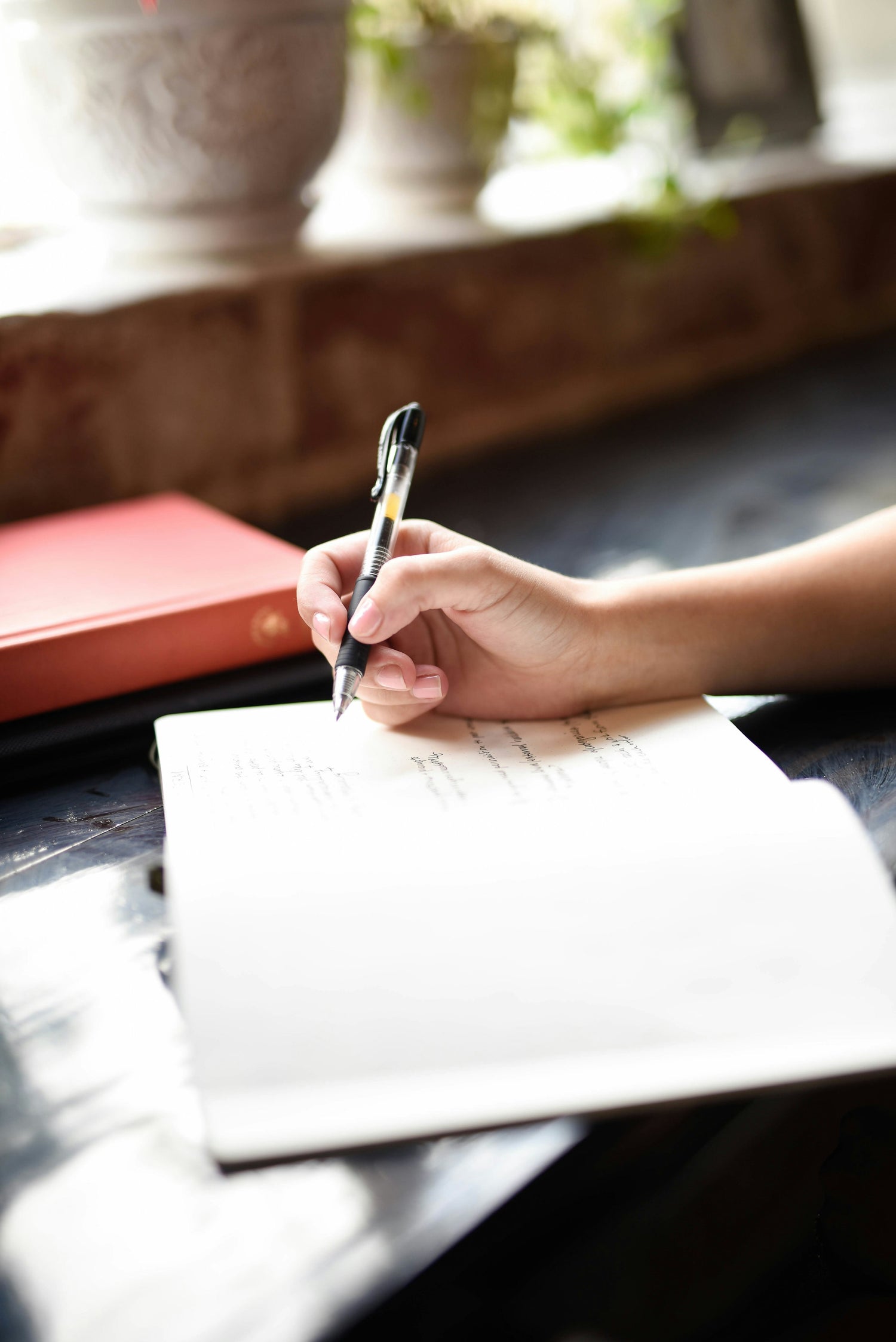 Close-up of a hand writing in a journal on a sunny windowsill, promoting mindfulness, reflection, and the journaling practice encouraged by The Microdose Journal.