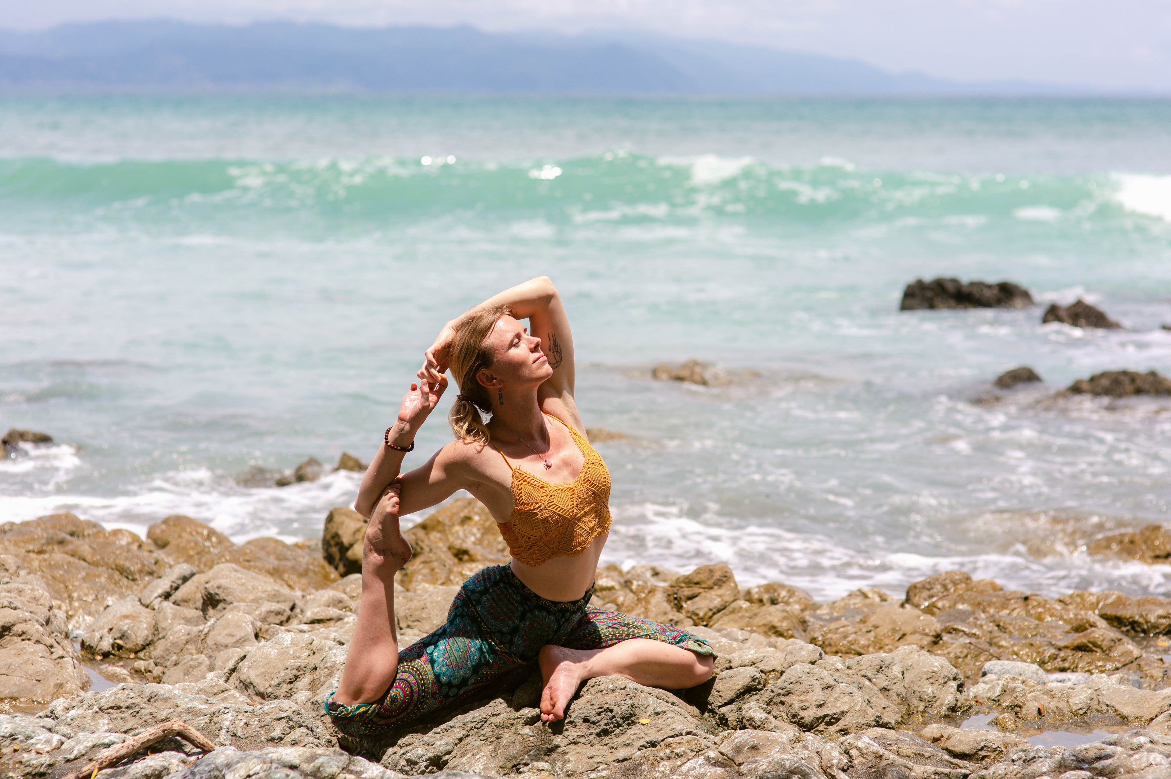 Steph Nally, yoga and meditation instructor, practicing yoga on rocky shores with ocean waves in the background, representing mindfulness, self-reflection, and balance.